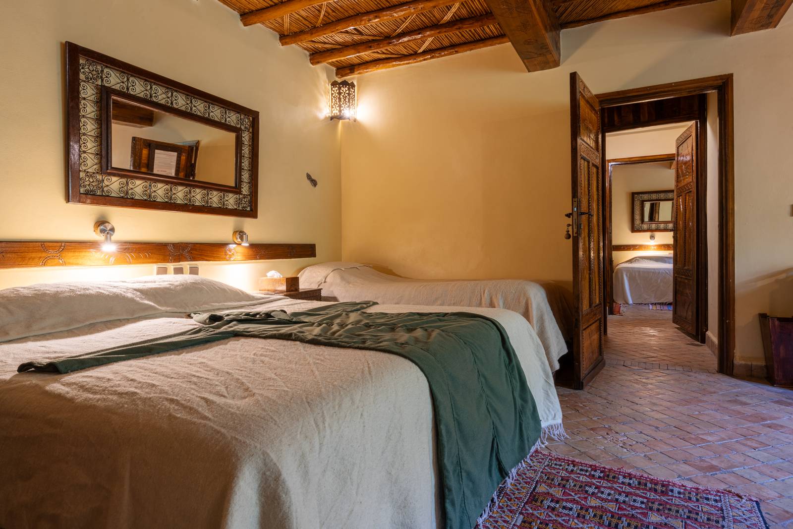 Chambre de l'Apartment Suite, trois lits sous un plafond de roseaux, porte en bois sculpté ouvrant sur une seconde chambre