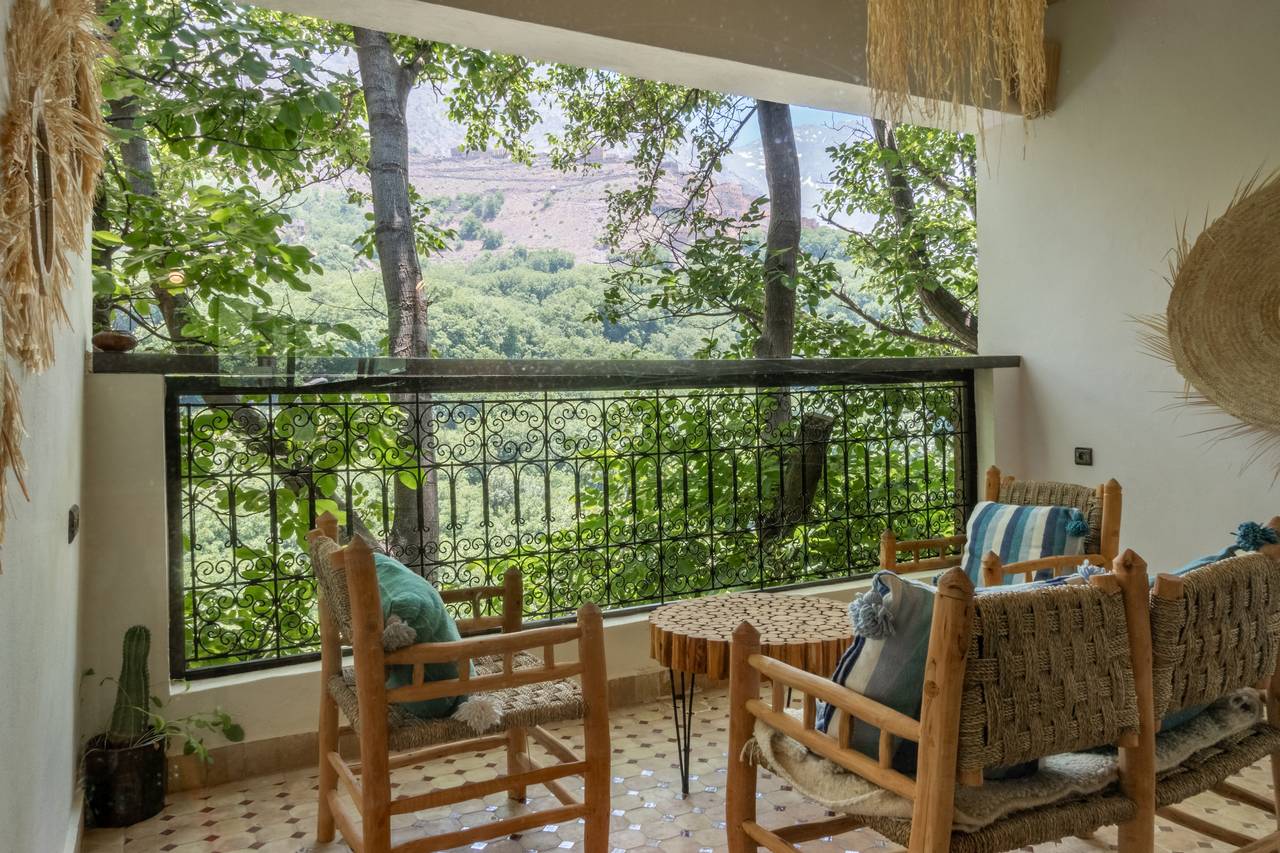 Balcon couvert d'une chambre Deluxe Plus, fauteuils en corde tressée et garde-corps en fer forgé ouvrant sur les noyers de la vallée