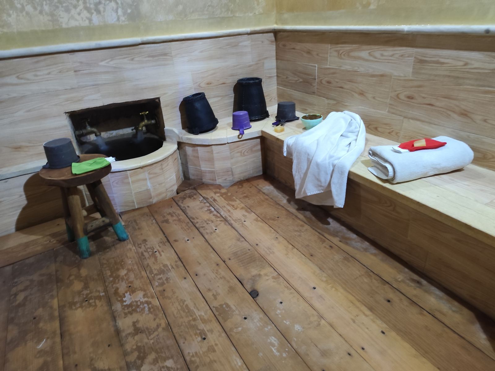 Salle humide du hammam, seaux traditionnels alignés sur le banc de bois et robinets de cuivre
