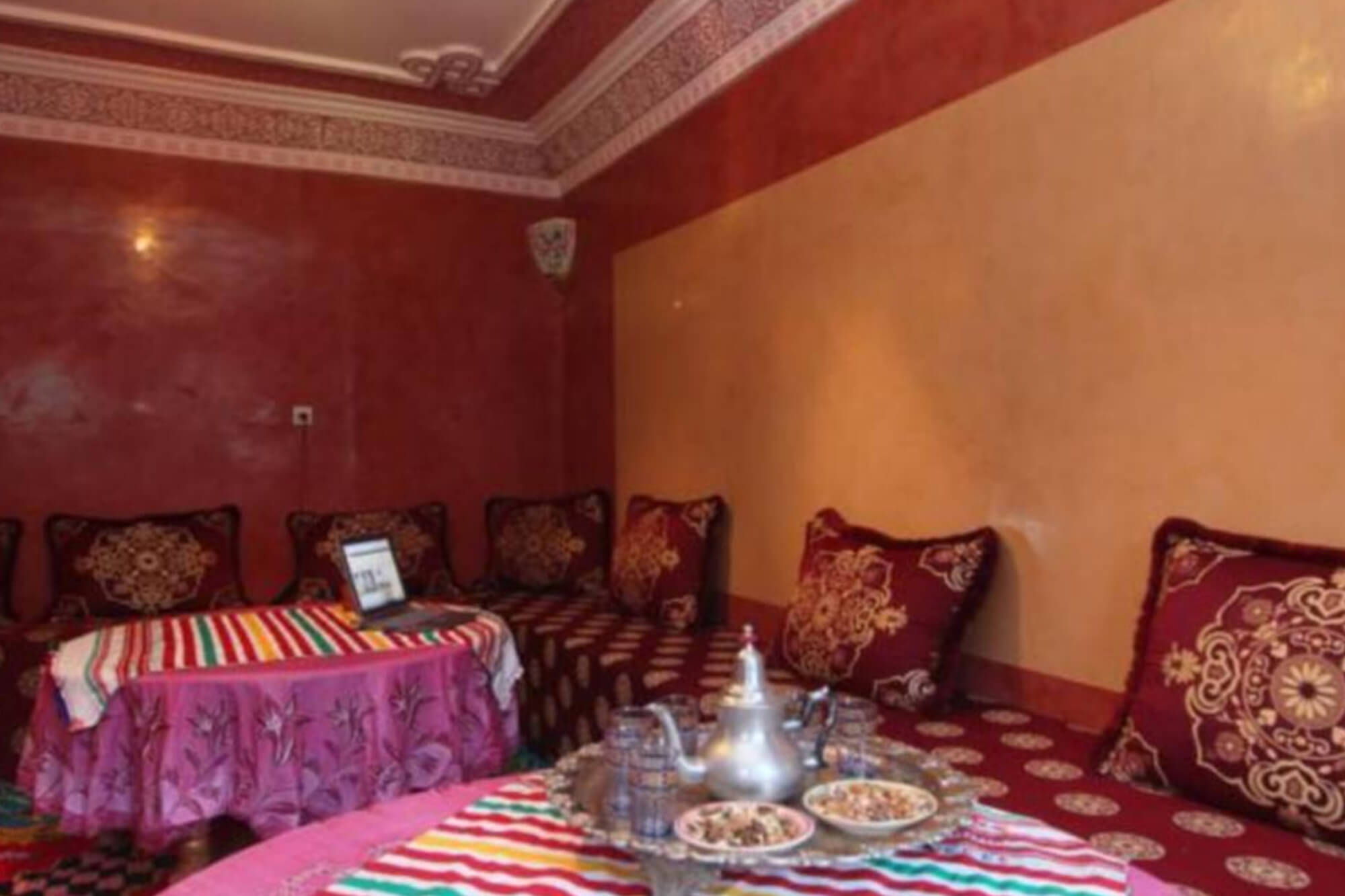 Salon aux murs rouge et ocre, banquettes garnies de coussins brodés et tables basses