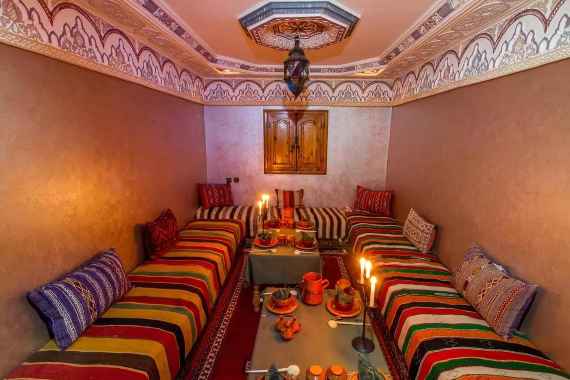 Salle à manger aux banquettes rayées, tables dressées et bougies sous un plafond à moulures peintes