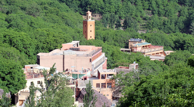 imlil Le fond de la vallée cultivé et vert entre des versants secs, vu depuis la route, un muret de pierre au premier plan