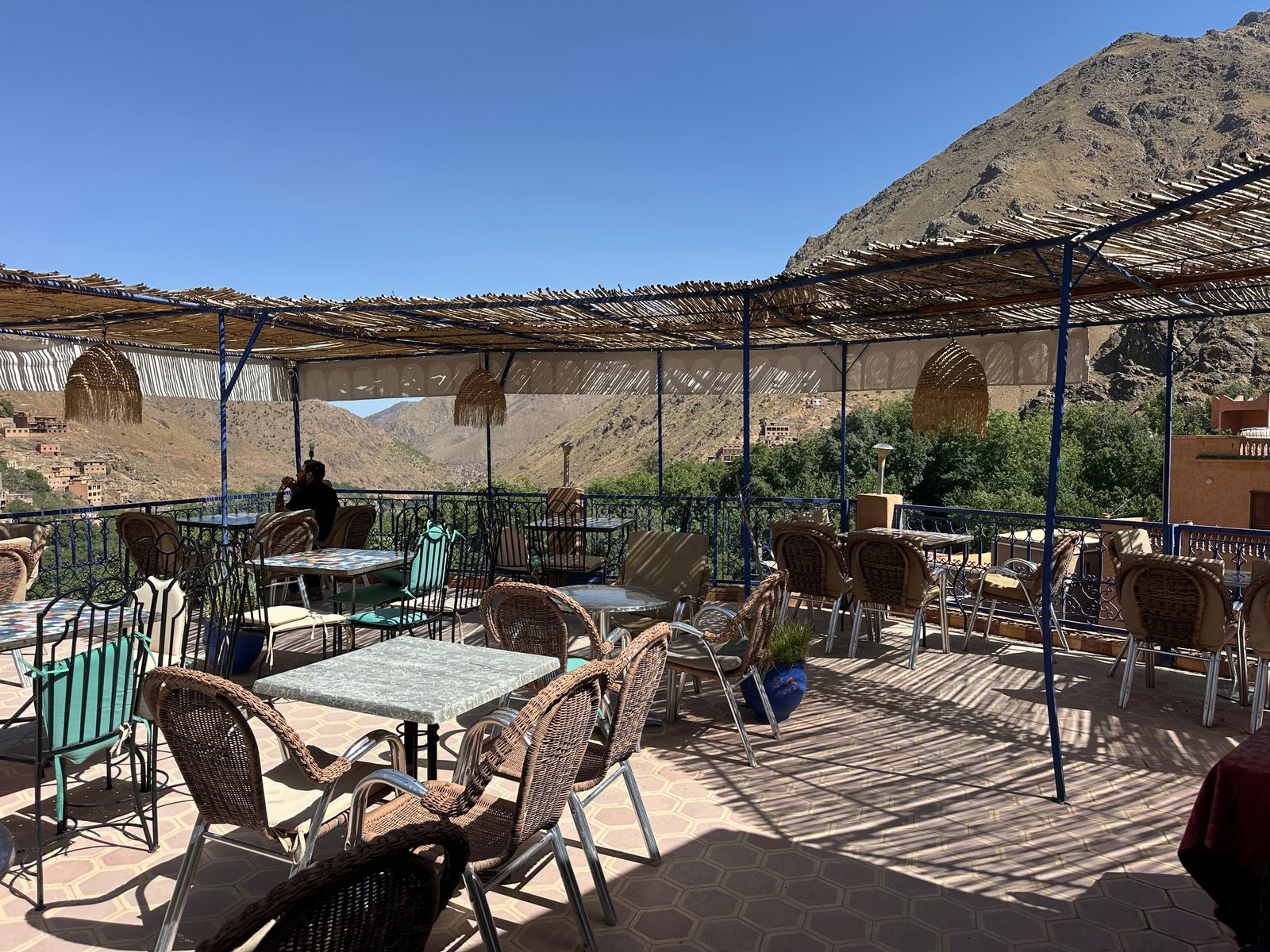 La terrasse sous sa pergola de roseaux, fauteuils d'osier et tables rondes, face au versant sec qui ferme la vallée