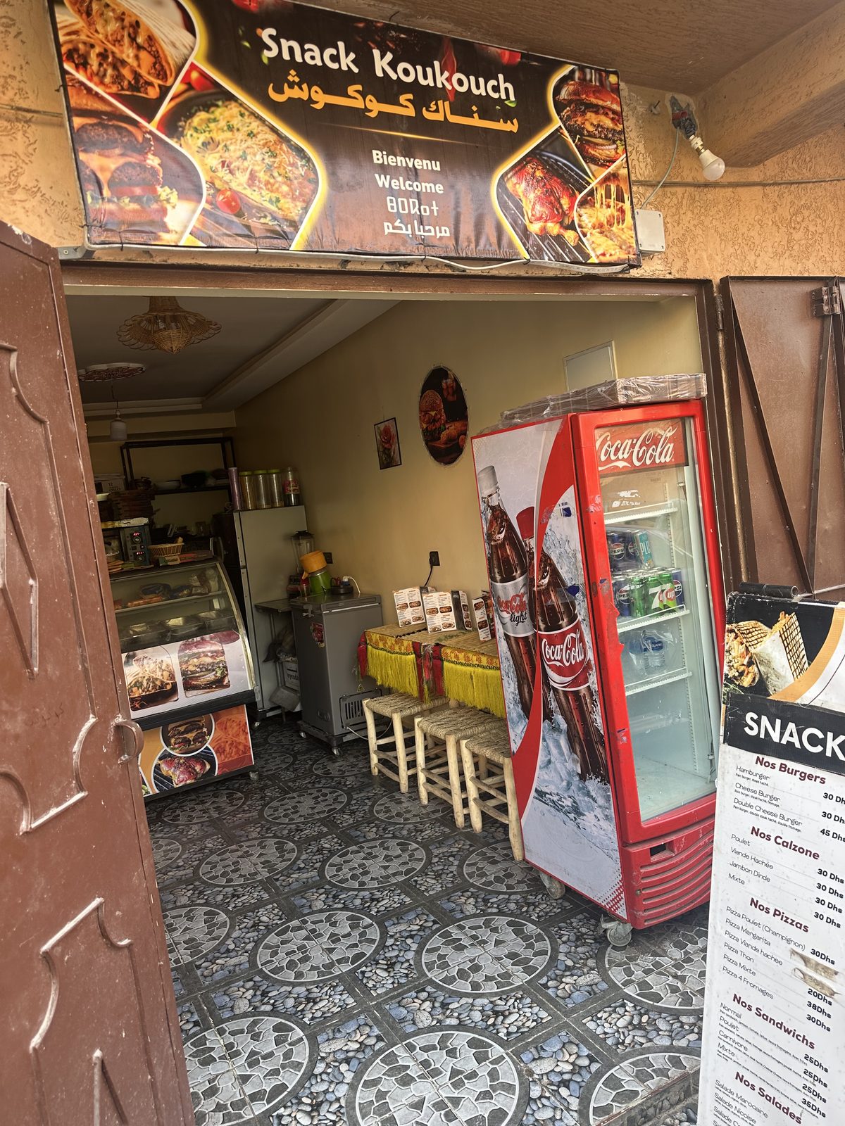 L'entrée vue depuis la rue, porte métallique ouverte sur la salle carrelée