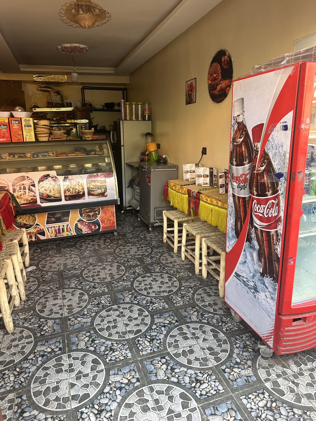 L'intérieur du snack : tables basses et tabourets tressés le long du mur, réfrigérateur à boissons et machine à jus au fond